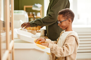 Poster - Side view portrait of teenage boy putting household waste in recycling bins at home, copy space