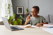 © Seventyfour - Portrait of smiling African-American boy wearing glasses watching online lessons while studying at home, homeschooling concept, copy space