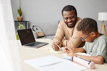 Wall Mural - Portrait of smiling African-American father helping son with homework while studying at home, copy space