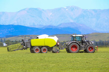A Tractor And Hay Baler Working In A Farm Field In Rural Canterbury, New Zealand
