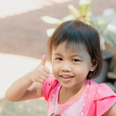 Wall Mural - Asian girl showing her thumbs up cheering up with happiness and looking at camera.