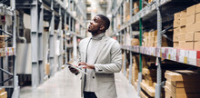 Portrait Of Smiling African American Business Man Order Details On Tablet Checking Goods And Supplies On Shelves With Goods Background In Warehouse.logistic And Business Export