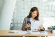 © PaeGAG - Female entrepreneur works and sits at workplace desk in office hold smartphone, prepare document agreement check details, read contract terms and conditions.