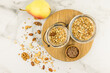 top view of two glass jars with muesli or granola on a wooden board and a marble table with scattered nuts and raisins. proper nutrition.
