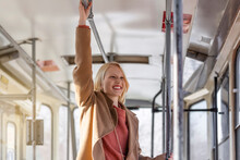 Young Woman Holding Handle While Moving In The Old Tram. Happy Passenger Enjoying Trip At The Public Transport