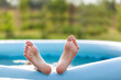 © Volha Zaitsava - Closeup of bare feet sprinkled water, sticking out of an inflatable pool in nature. Child staying cool in the summer heat.