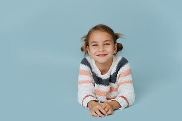 Cheeky little girl in striped sweater lying on the floor over blue background