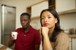 © Anatoliy Karlyuk - Selective focus of African couple, sitting at kitchen in morning, man on background holding white coffee cup, thoughtful woman with hand under chin, contemplating, getting ready to go for work