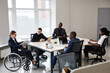 © Seventyfour - Portrait of successful businesswoman using wheelchair while leading business meeting in office with diverse group of people, copy space