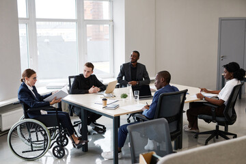 Portrait of successful businesswoman using wheelchair while leading business meeting in office with diverse group of people, copy space