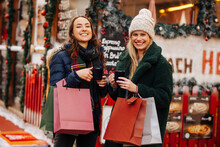 Cheerful friends with shopping bags enjoying mulled wine at Christmas market