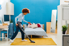 Afro Young Woman Cleaning Carpet With Vacuum Cleaner In Bedroom At Home