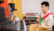 © princeoflove - Asian musician streaming his live concert on social media. Male guitarist recording guitar track on computer in home studio. Music teacher streaming guitar lesson for teaching his student on internet
