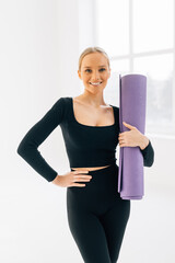 Wall Mural - Beautiful smiling young girl in sportswear holding a yoga mat isolated on white background. Healthy lifestyle concept. Fitness and yoga concept.