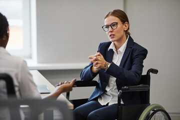 Portrait of young businesswoman using wheelchair while speaking to colleague in meeting, copy space