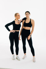 Wall Mural - Portrait of two fit young women standing over white background