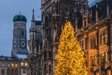 Germany, Bavaria, Munich, Christmas Tree Glowing On Marienplatz At Dusk With Cathedral Of Our Lady And Town Hall In Background