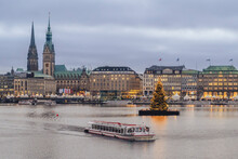 Germany, Hamburg, Tourboat Sailing Across Inner Alster Lake With Christmas Tree And City Buildings In Background