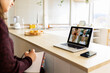 © Westend61 - Young working woman with notebook doing video call with colleagues on laptop at home