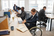 © Seventyfour - Side view portrait of smiling businesswoman using wheelchair while working with colleague in office, copy space