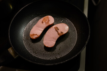 Two sausages are fried in a pan.