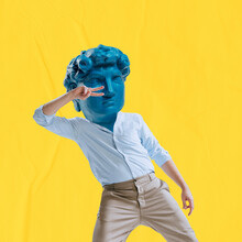 Young Man Headed By Blue Statue Head Dancing Isolated On Yellow Background. Contemporary Colorful And Conceptual Bright Art Collage