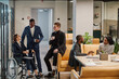 © Seventyfour - Full length portrait of diverse business team with young woman in wheelchair chatting to colleagues in office