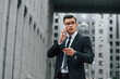 © standret - Using phone. Businessman in black suit and tie is outdoors in the city