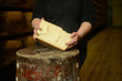 woman cutting and holidng a slice of a hard matured parmesan cheese wheel in diary farm production storage