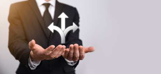 Male hand holding icon with three directions icon on dark background. Doubt, having to choose between three different choices indicated by arrows pointing in opposite direction concept. Ways