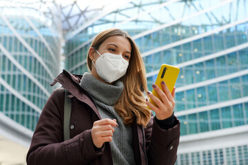 Wall Mural - Business woman covering face with protective mask holding mobile phone with modern city background. Technolgy, growth, health care concept.