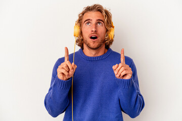 Wall Mural - Young caucasian man listening to music isolated on white background pointing upside with opened mouth.