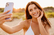 © Drobot Dean - Young brunette woman smiling while taking selfie photo on cellphone