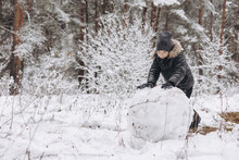 Happy Child Rolling Big Snowball For Snowman In Snowy Winter Forest. Teenager Boy Playing And Having Fun On Walking In Frosty Day. Wintertime Activity Outdoors.
