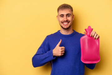 Wall Mural - Young caucasian man holding a water bag isolated on yellow background smiling and raising thumb up