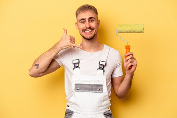 Young painter man isolated on yellow background showing a mobile phone call gesture with fingers.