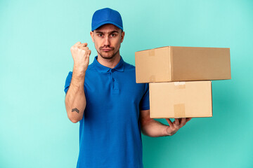 Wall Mural - Young delivery caucasian man isolated on blue background showing fist to camera, aggressive facial expression.