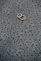 two gold wedding rings against a background of glossy black metal covered with raindrops