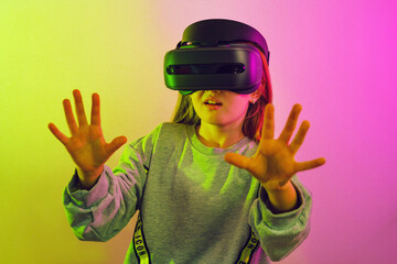 Wall Mural - girl 7 y.o. experiencing vr headset game on pink background. child using a gaming gadget for virtual