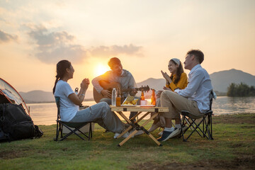 Wall Mural - happy group of Asian friends Play guitar and sing enjoying camping and drinking beer