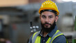 © eakgrungenerd - Portrait of man engineer wear yellow helmet and uniform standing at industrial workshop. handsome workman with beard on face ​in factory. Copy space.