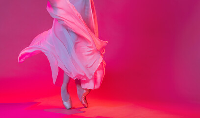 Wall Mural - Legs of a ballerina in pointe shoes stand on a pink background
