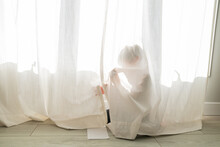 Young Child Hiding Behind A Curtain At Home
