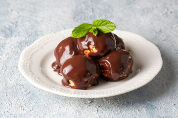 Wall Mural - Delicious profiteroles with chocolate and white plate. Selective focus image on light background.