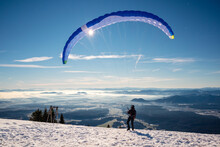 Paragliding In Mountains, Winter Time With Snow And Blue Sunny Sky.