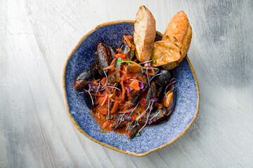 Mussels in tomato sauce with spices and lemon on beautiful plate on grey table