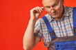 © Aleksandr - A bald, bearded man in work clothes and protective glasses looks indignantly at the camera, a photo on a red background. The main builder checks the work of subordinates.