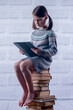 Portrait of young girl sitting on stack of books with PC tablet. Concept of learning new knowledge, self improvement and development of mental abilities. Vertical image.