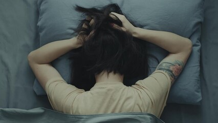 Wall Mural - A woman lies buried in a pillow in bed, pressing her hands to her head. Headache or migraine concept.