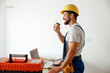 © Kostiantyn - Side view of smiling handyman in uniform and hard hat drinking coffee during a break while doing renovation work indoors